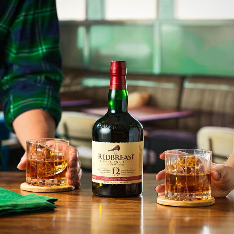 A bottle of Redbreast 12 next to two old fashioned cocktails.